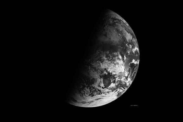 A black and white Earth on the right gives way to a planet in shadow on the top left side.