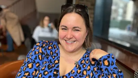 Lisa Clavering Lisa Clavering is pictured in a blue leopard print top while smiling in a coffee shop
